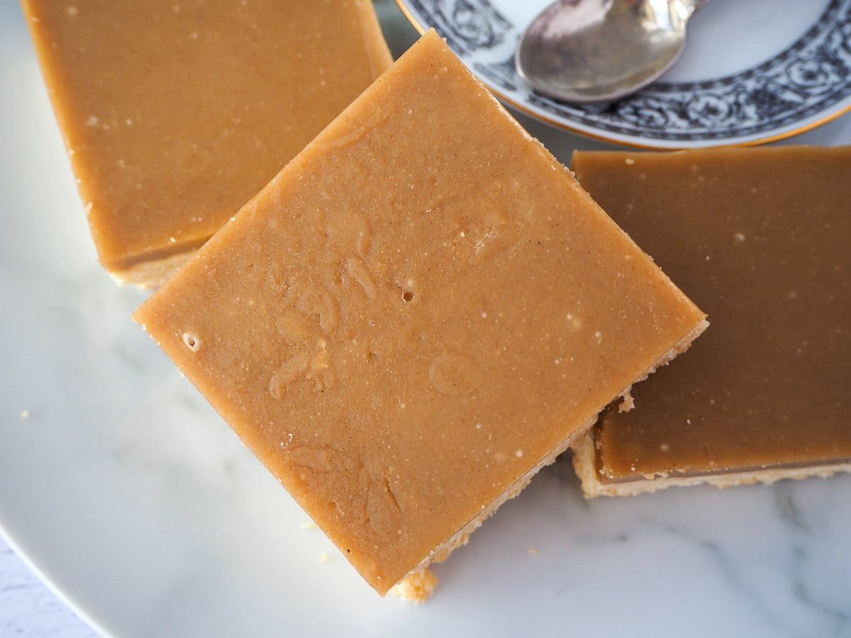 Close up of piece of ginger crunch stacked on top of other pieces, with a coffee saucer to the side.
