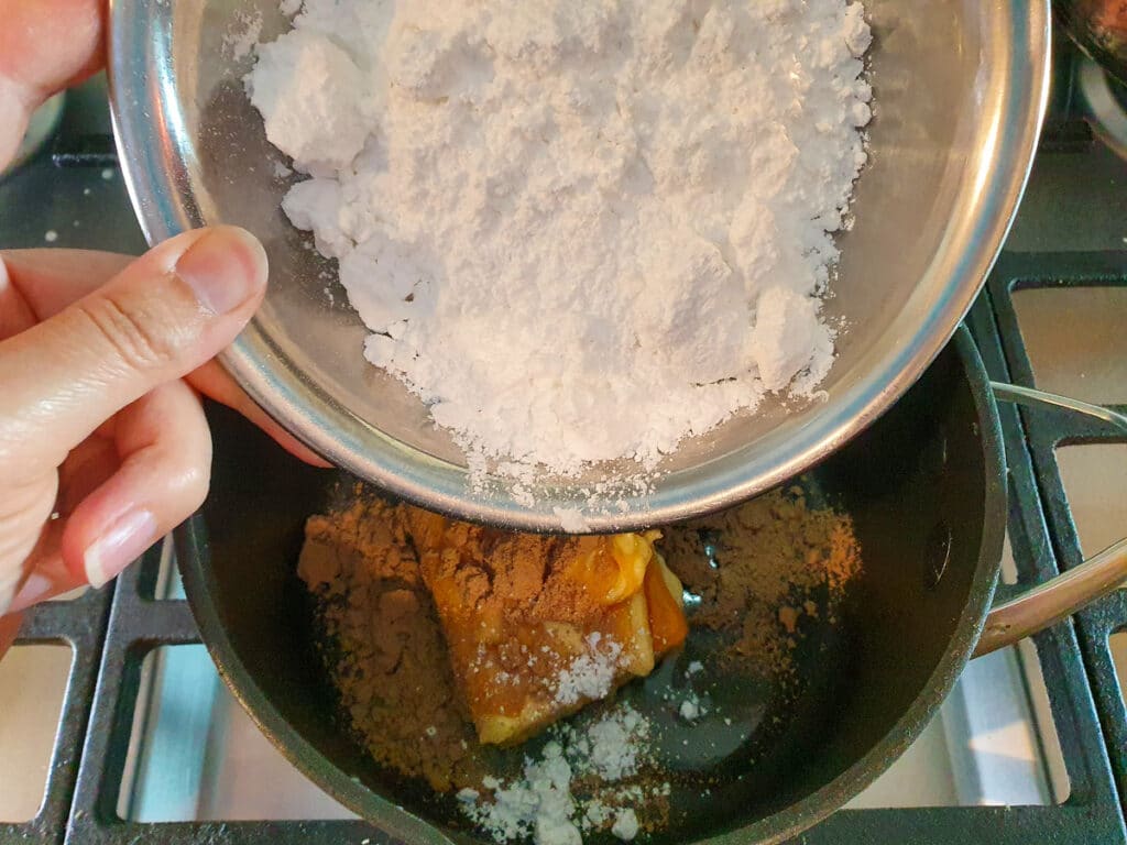 Adding sifted icing sugar to icing in pot on stove.