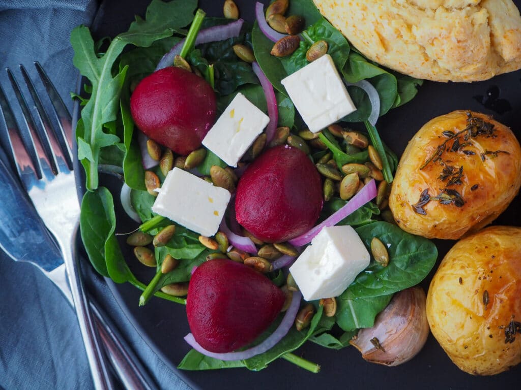 Beetroot salad 13 Beetroot salad on a plate, served with damper and roasted mini potatoes and cutlery on the side.