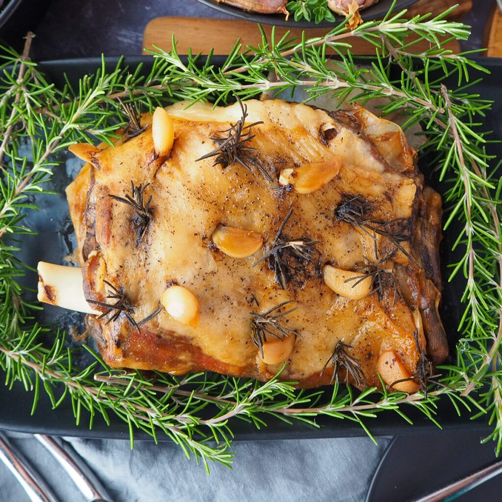 90 Dirt cheap meals 91 Close up slow cooker lamb roast on a serving plate, garnished with fresh rosemary.