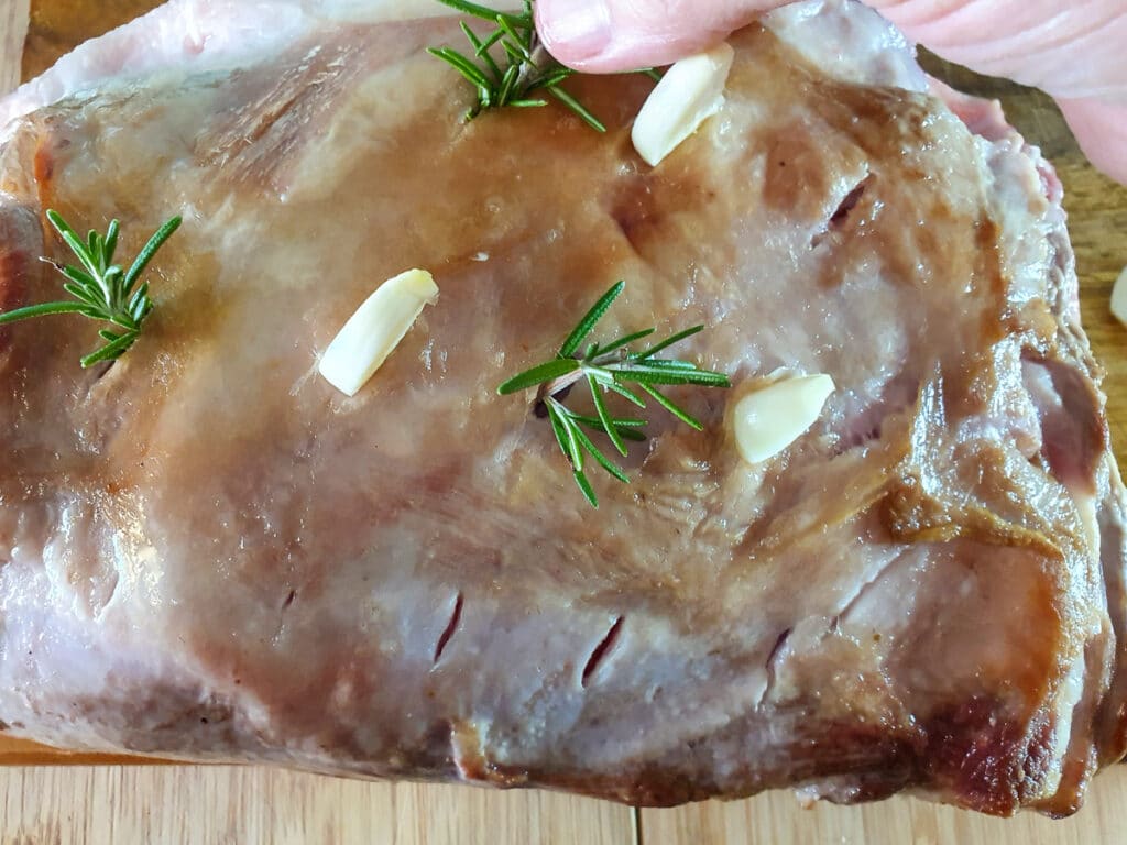 Inserting rosemary sprigs into cut slits in roast.