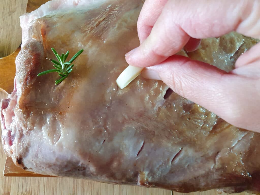 Inserting garlic sprigs into cut slits in roast.