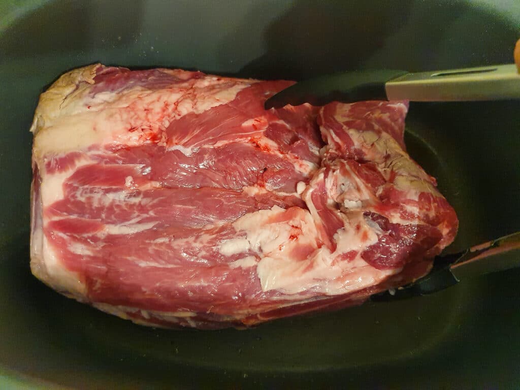 Turning the lamb over with tongs.