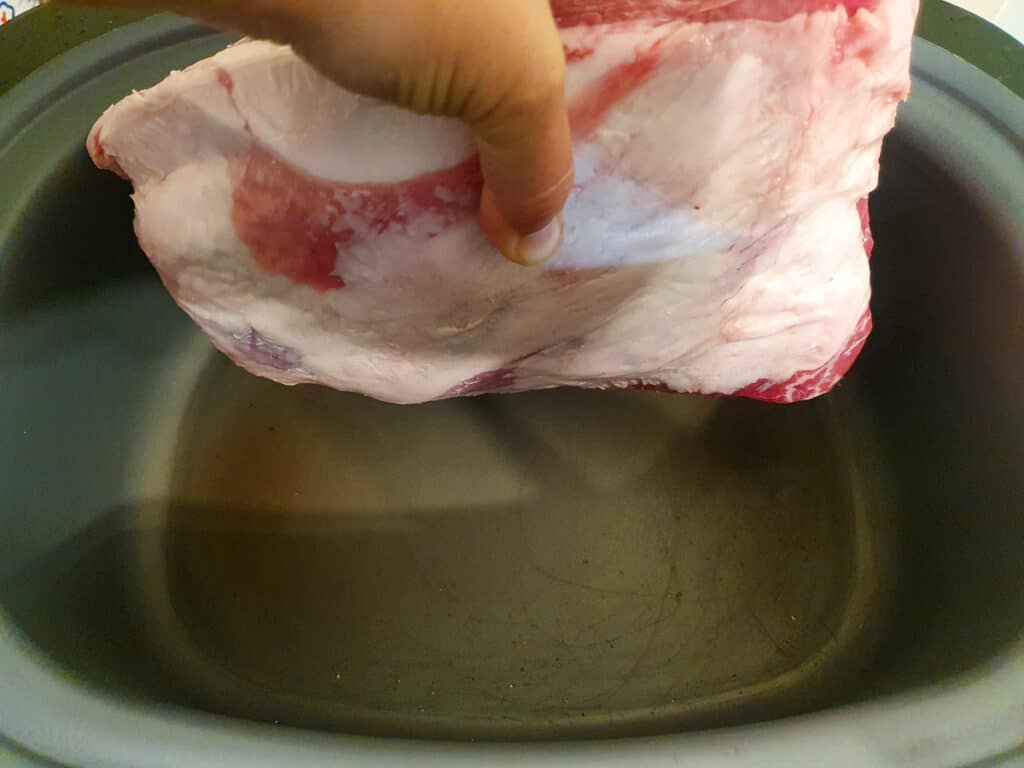 Putting the lamb into the heated searing slow cooker, fat side down.