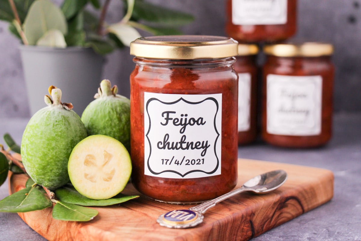 Feijoa chutney 1 jar of homemade feijoa chutney on a board, with vintage spoon and fresh feijoas, stacked jars of chutney in the background.