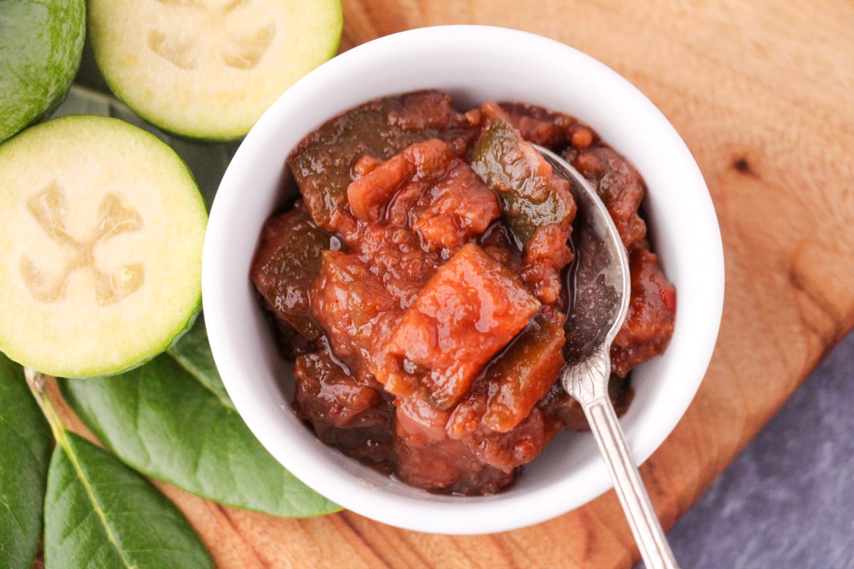 Feijoa chutney 3 Feijoa chutney in a serving bowl on a bowl with a serving spoon, on a board with fresh feijoas and feijoa leaves.