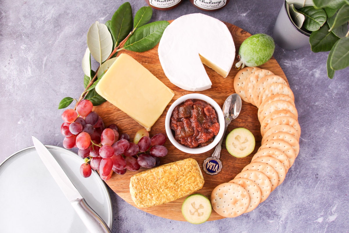 Feijoa chutney 16 Cheeseboard with feijoa chutney, serving plate and knife, jars of chutney and fresh feijoa leaves on the side.
