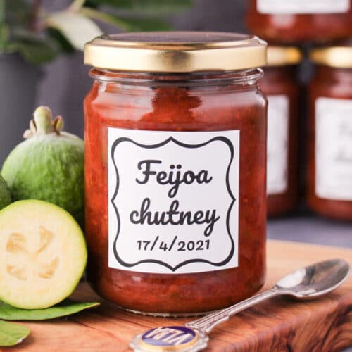 Feijoa chutney 31 Close up jar of homemade feijoa chutney on a board, with vintage spoon and fresh feijoas, stacked jars of chutney in the background.