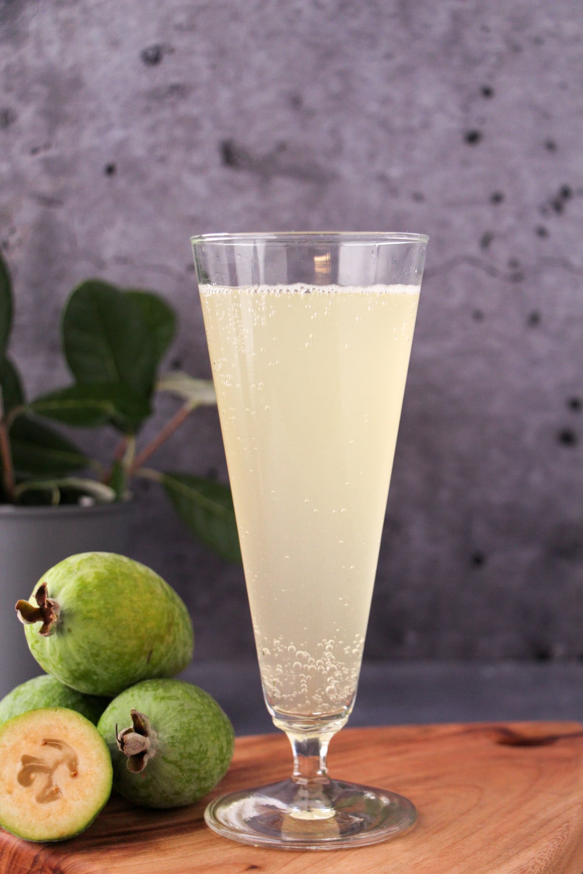 Tall glass of feijoa fizz on a board, with fresh feijoas and feijoa leaves.
