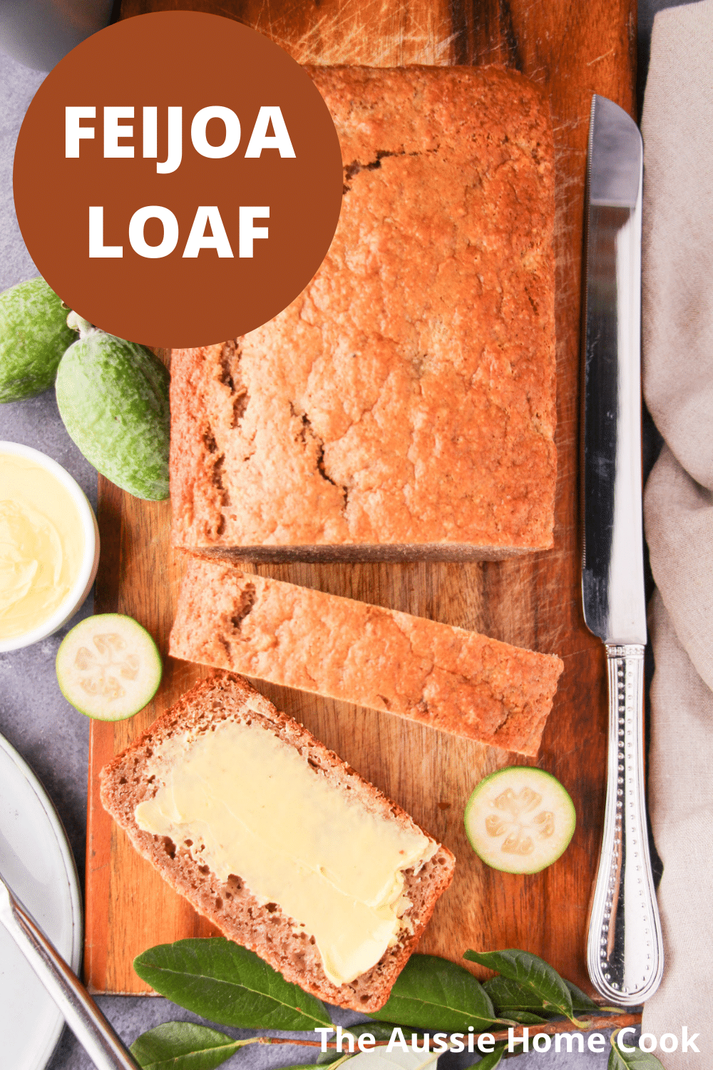 Sliced feijoa loaf on a chopping board, with one buttered slice, fresh feijoas and leaves, large cutting knife, butter and plate and knife on the side, with text overlay, feijoa loaf and The Aussie Home Cook.