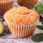Close up feijoa muffins with fresh feijoas and feijoa leaves, with extra muffins on a cooling rack in the background.