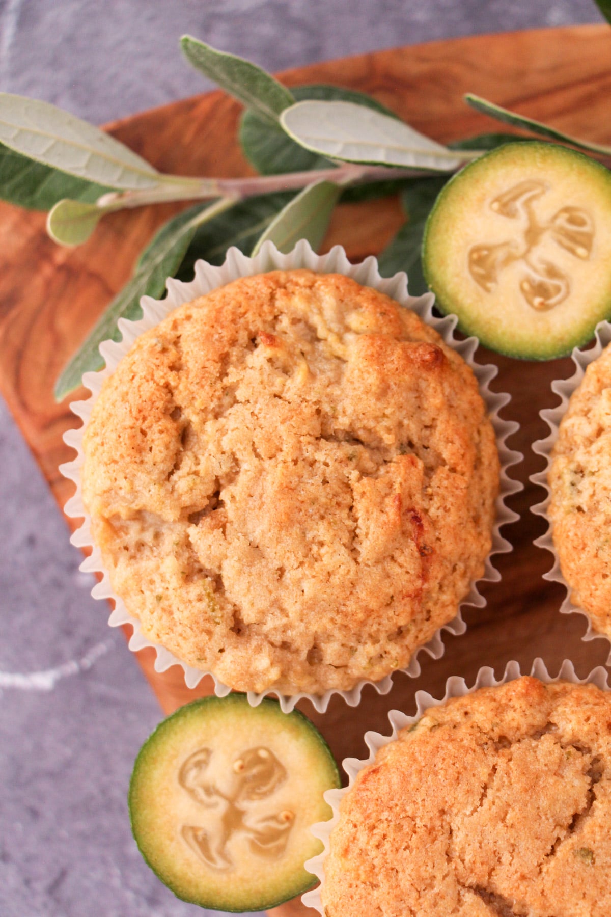 Feijoa muffins on a board with fresh feijoas and feijoa leaves.