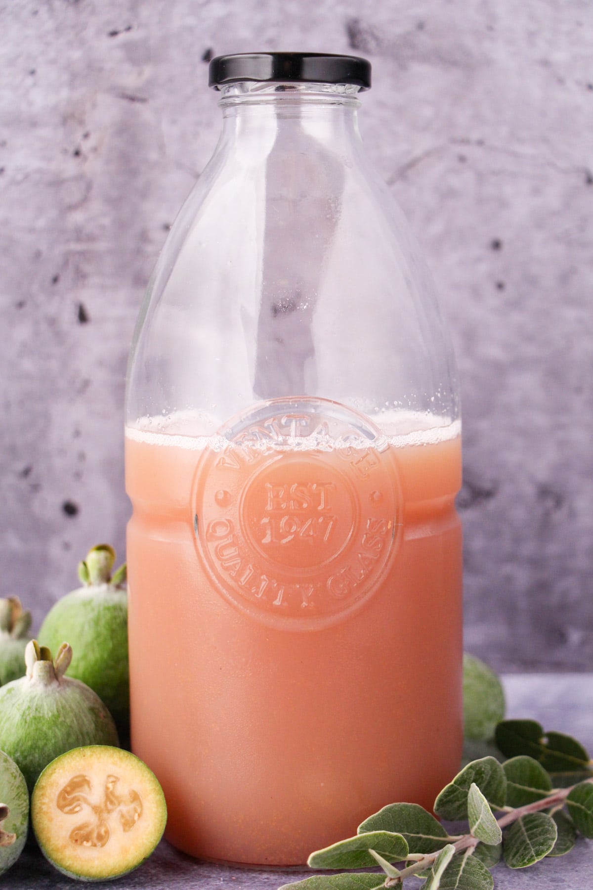 Bottle of feijoa syrup withy fresh feijoas and leaves.