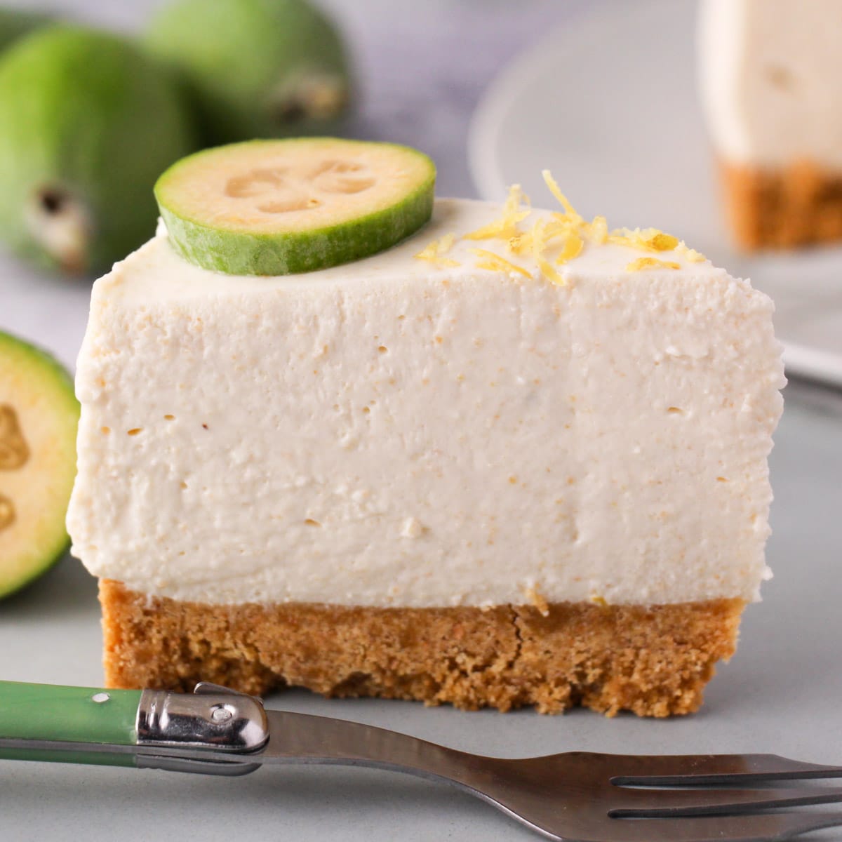 Slice of feijoa cake on the serving plate with vintage spoon, rest of cake and fresh feijoas in the background.