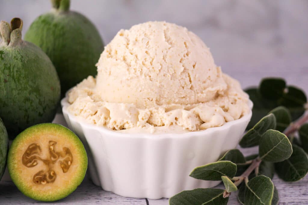 Scoop of feijoa ice cream with fresh feijoa, vintage spoon and sprig of feijoa leaves.