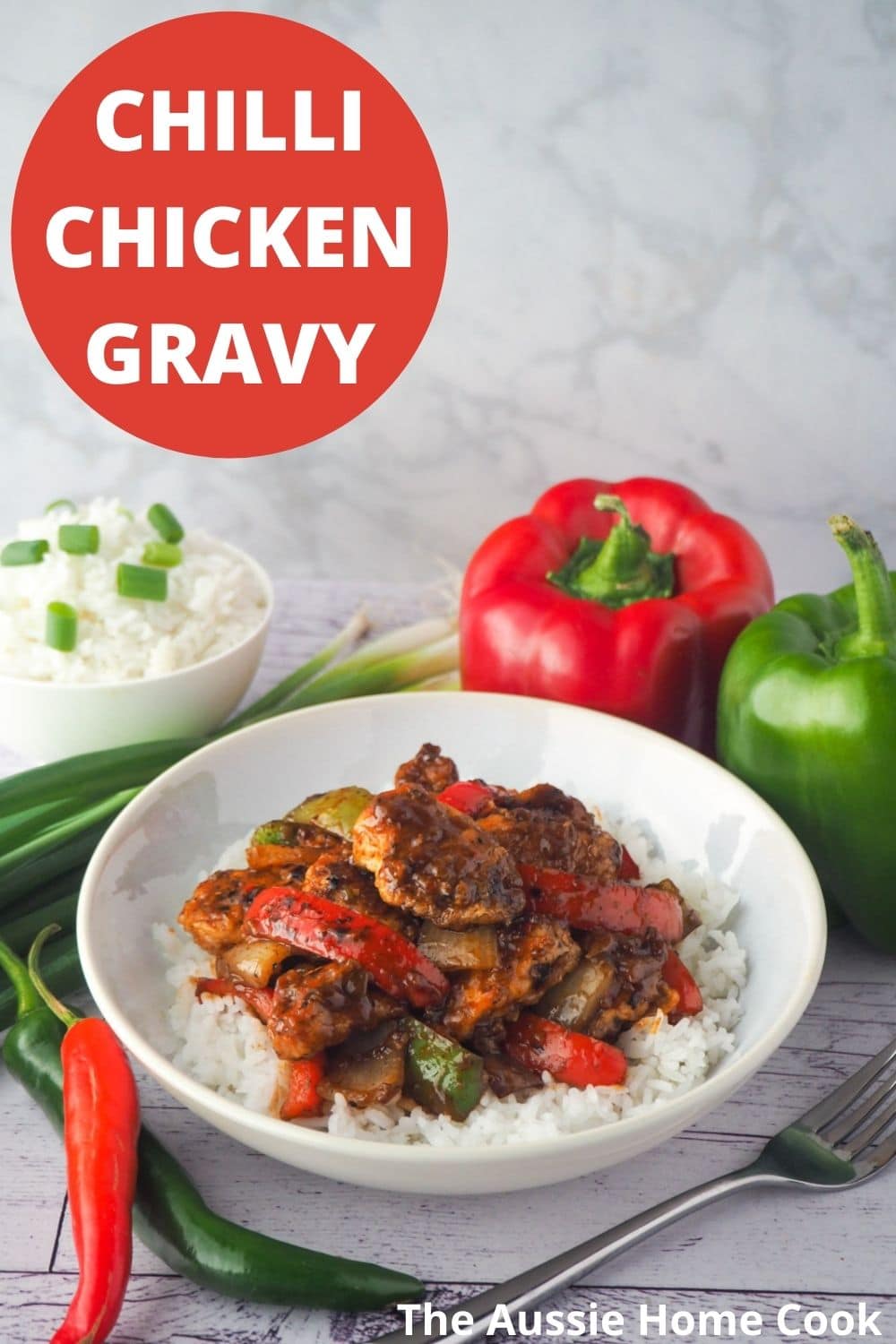 Bowl of chicken on rice with fork and capsicums, spring onions and chilli on the side with text overlay, chilli chicken gravy and The Aussie Home Cook.