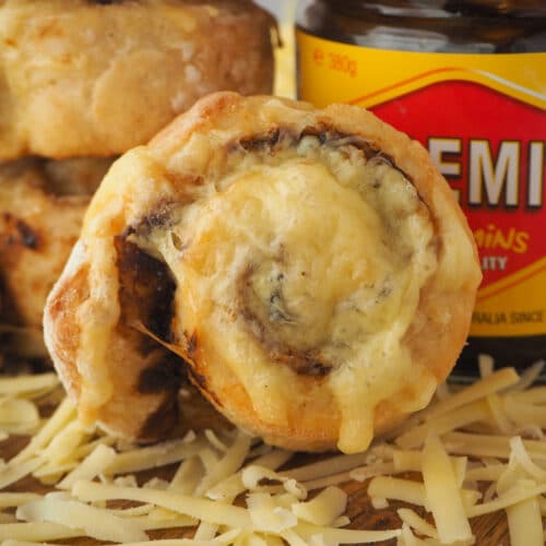 Cheesymite Scrolls 24 Close up scroll with stack of scrolls and jar of vegemite behind it.