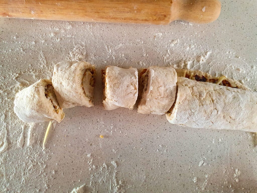 Cheesymite Scrolls 12 Slicing up rolled dough into eight pieces.