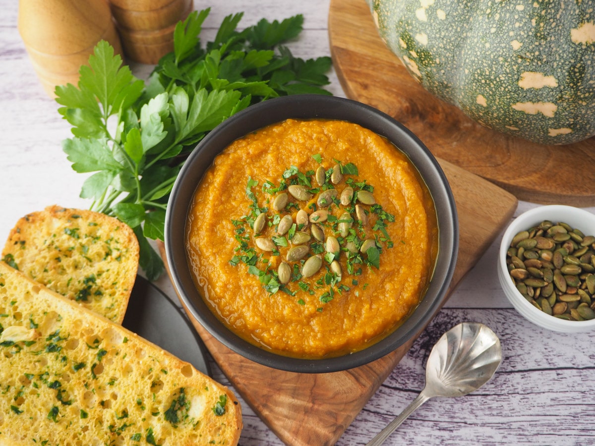 Pumpkin and Sweet Potato Soup 19 Soup with pumpkin seed and parsley garnish, with garlic bread, spoon and toasted pumpkin seeds on the side.