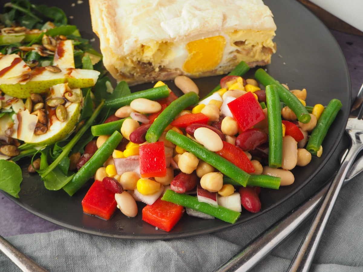 Four Bean Salad 12 Salad on a plate with a slice of pie, rocket and pear salad and knife and fork.