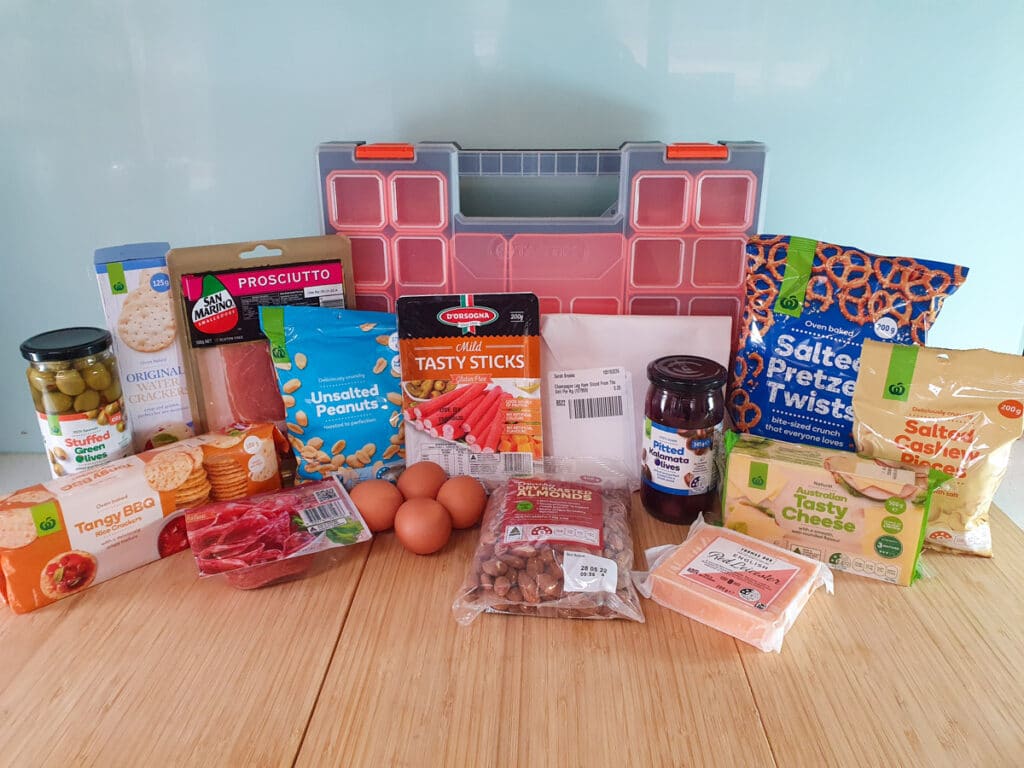 Picnic Charcuterie Board 2 Ingredients: green stuffed olives, BBQ rice crackers, plain water crackers, prosciutto, salami, peanuts, eggs, twiggy sticks, roasted almonds, ham, pitted Kalamata olives, red Leicester cheese, tasty cheese, salted pretzels, salted cashews, multi compartment tool box.