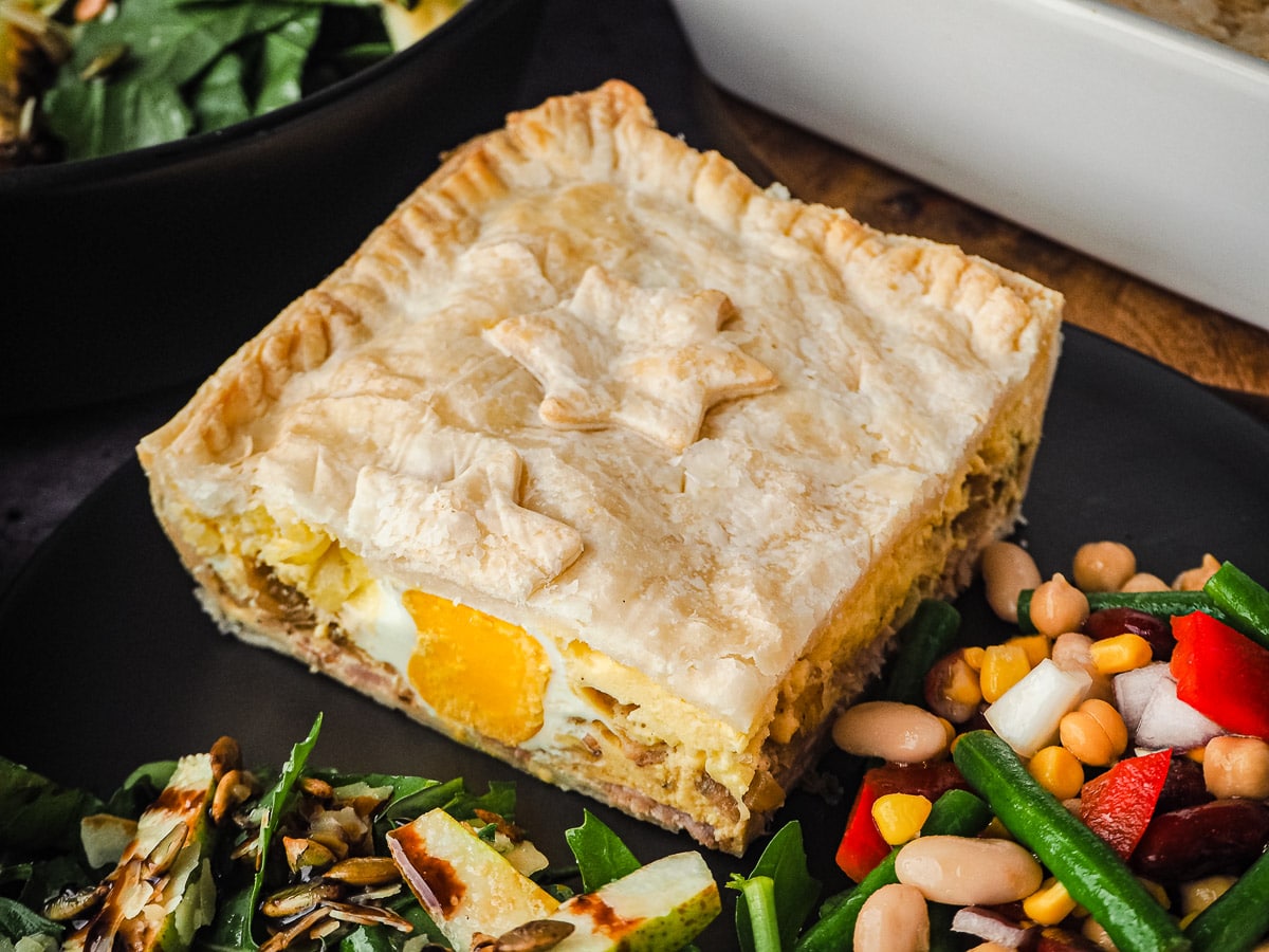 Pie in a plate with salads, with pie dish and salads in background.