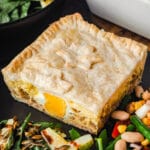 Close up pie in a plate with salads, with salads in background.
