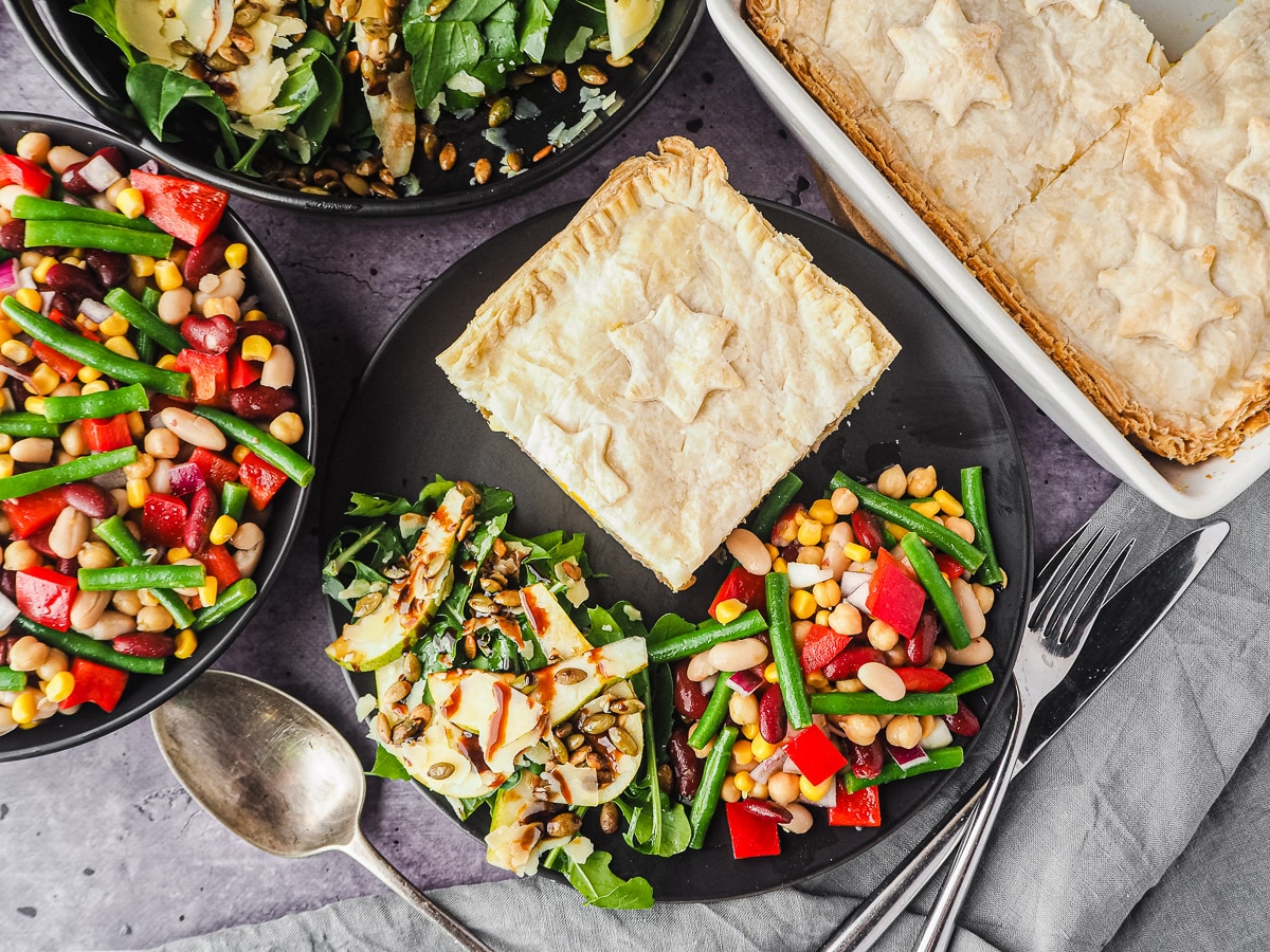 Pie in a plate with salads, with pie dish and salads in background.