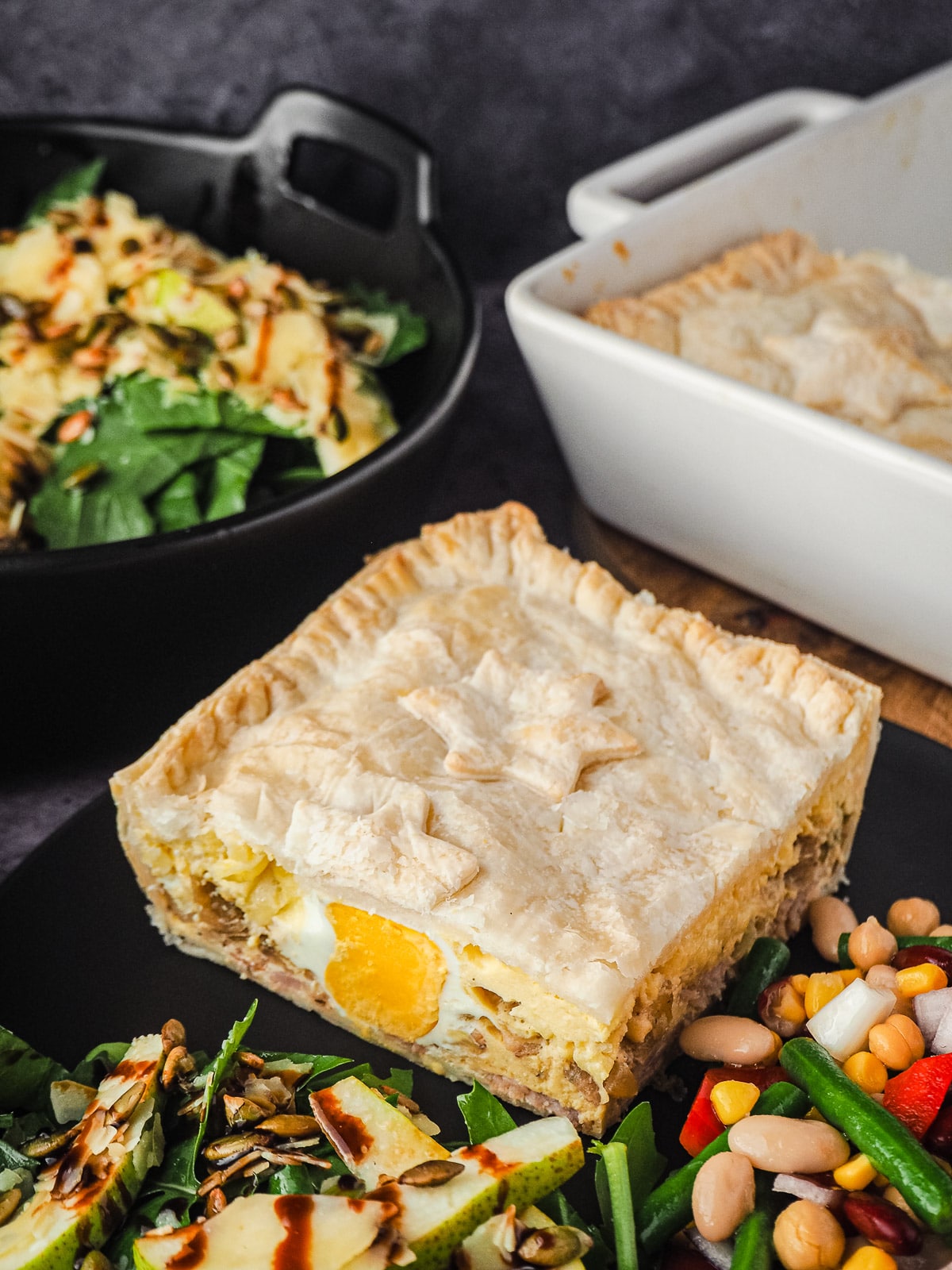 Pie in a plate with salads, with pie dish and salads in background.