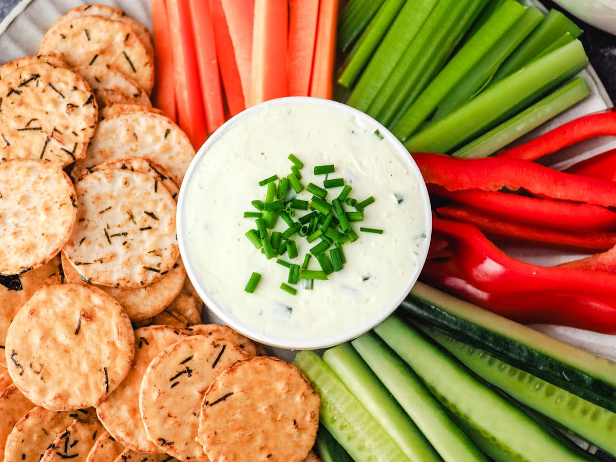 Sour cream dip with veggie sticks, carrots, celery, red pepper and cucumber, and rice crackers.