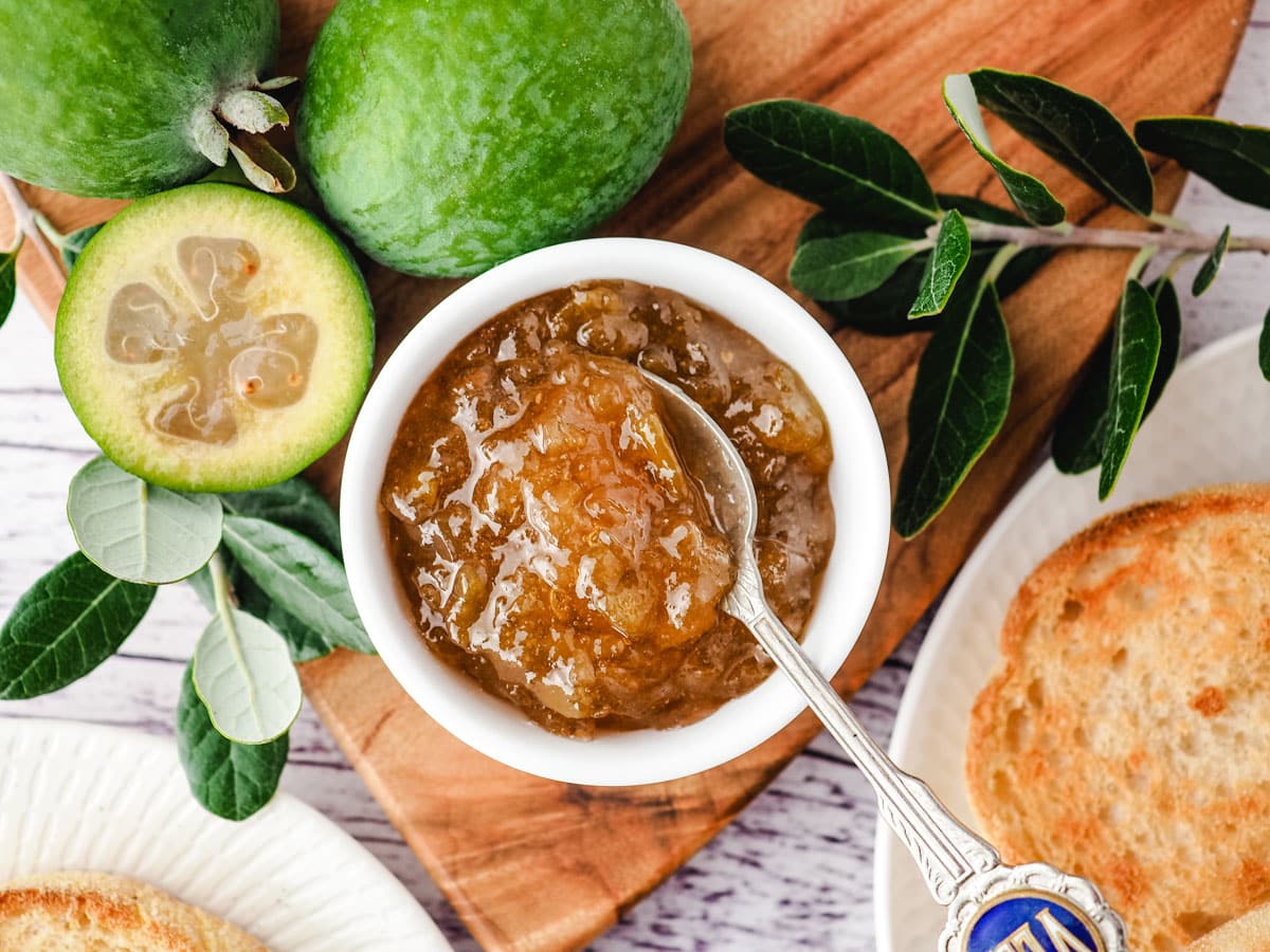 Feijoa Jam 7 Top down view of bowl of feijoa jam, with fresh feijoas and leaves and toasted English muffins on the side.