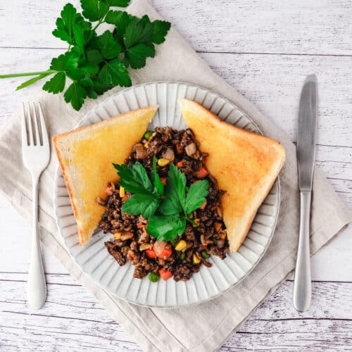 Savory Mince 15 Savory mince on a plate with buttered toast on the side, garnished with flat parsley, with a knife and fork on the side.