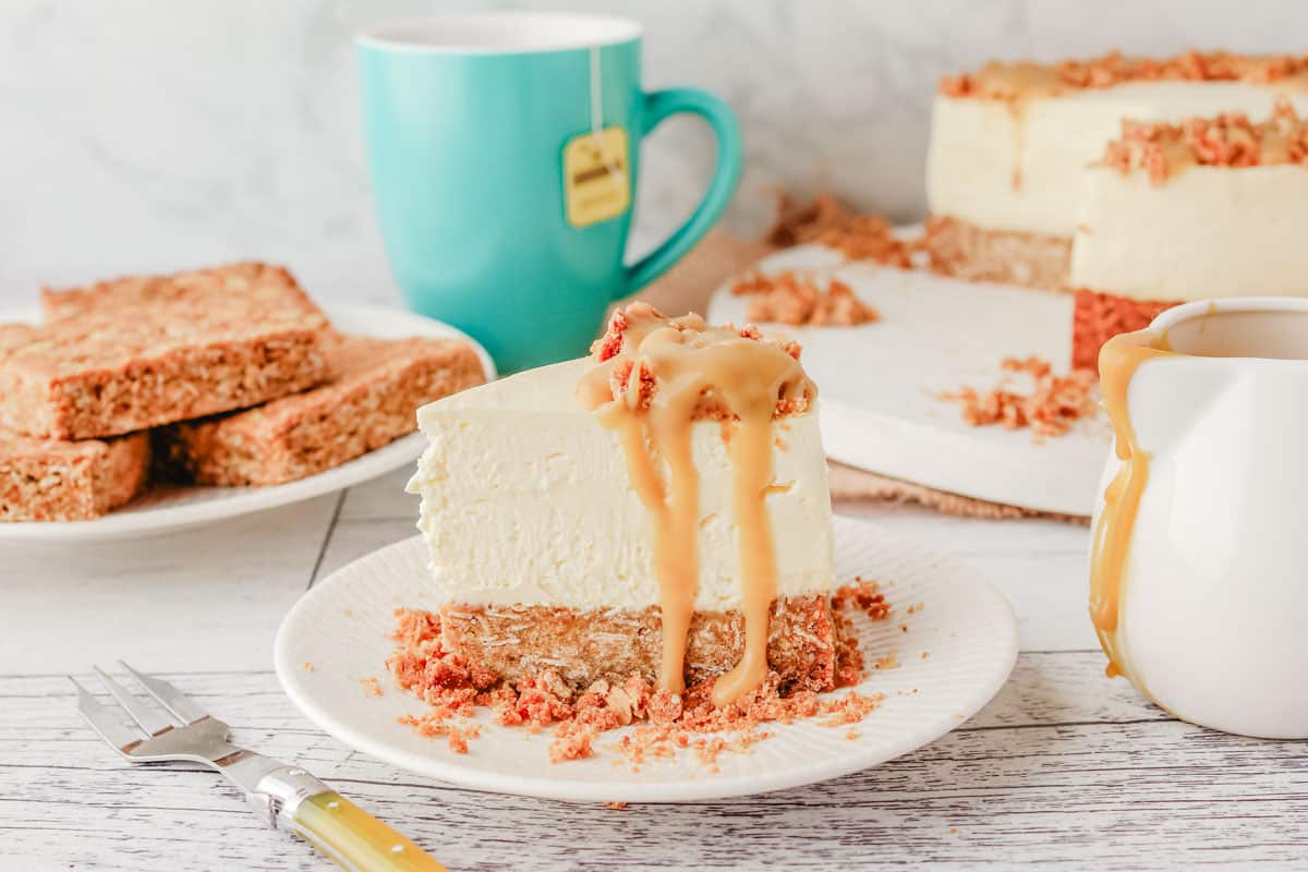 Slice of Anzac cheesecake with Anzac slice and rest of cheesecake in the background.