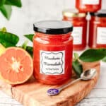 Mandarin Marmalade 7 Jar of mandarin marmalade on a serving board with a spoon, with freshly sliced open mandarin and leaves on the side.