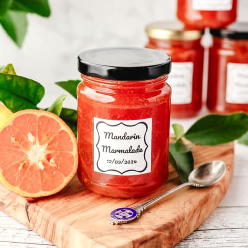 Mandarin Marmalade 29 Jar of mandarin marmalade on a serving board with a spoon, with freshly sliced open mandarin and leaves on the side.